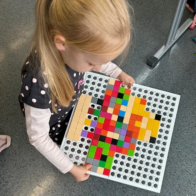 Mädchen betrachtet eine weiße Steckplatte mit bunten, pfeilförmig angeordneten Bauklötzen.