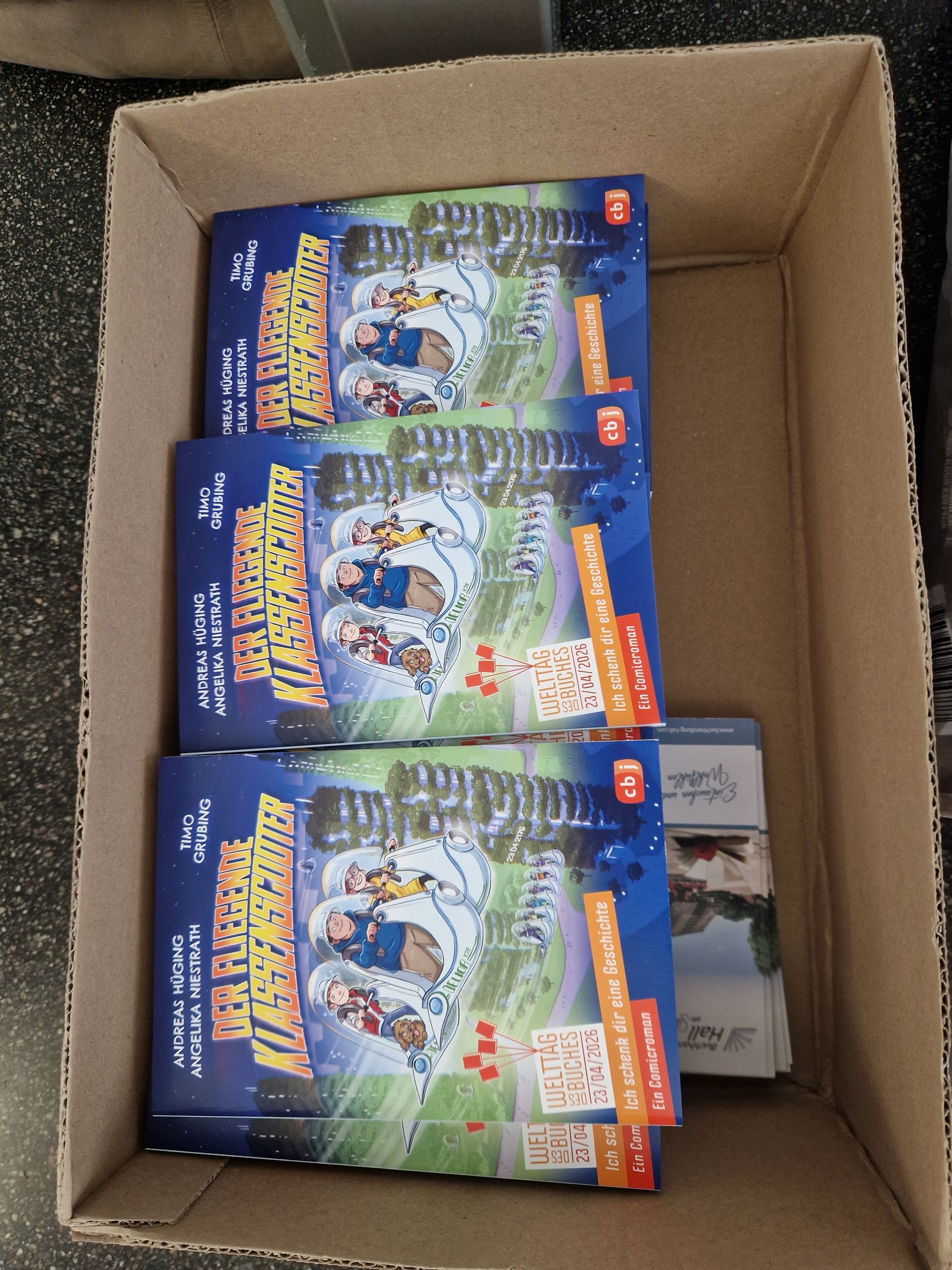 Open cardboard box holding three colorful Pokémon trading card booster boxes and two small packs