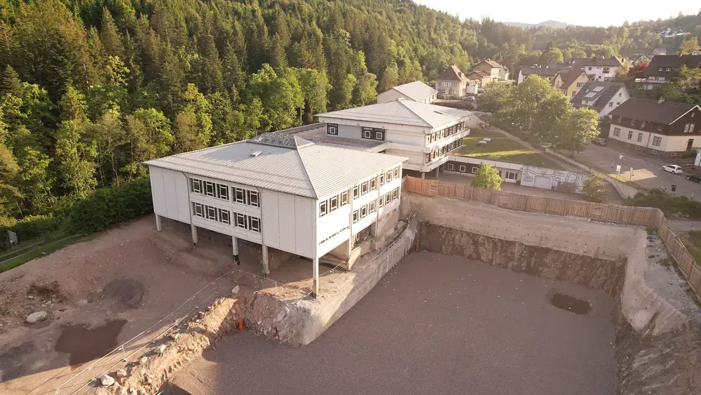 Luftaufnahme von im Bau befindlichen weißen Gebäuden neben einem bewaldeten Hang.