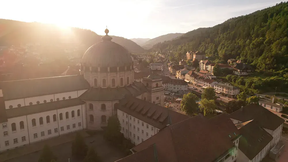 Luftaufnahme einer großen Kirche mit Kuppel, eingebettet in eine Talstadt bei Sonnenuntergang.