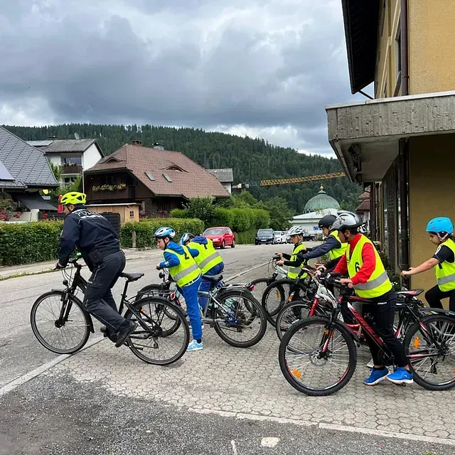 Radfahrer in gelben Westen, Fahrräder, in der Nähe eines Gebäudes. Bergkulisse, bedeckter Himmel.