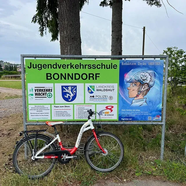 Ein Fahrrad ist vor einem grünen Schild einer Jugendverkehrsschule in Bonndorf, Deutschland, geparkt, auf dem eine Person mit Helm abgebildet ist.
