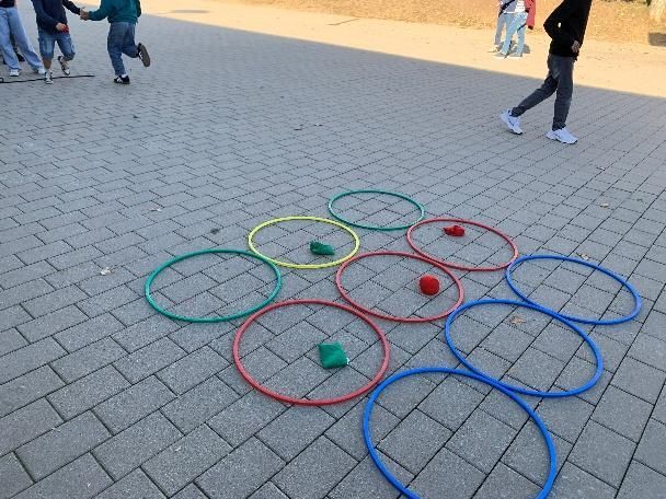 Colorful hoops and beanbags arranged on pavement during an outdoor game.