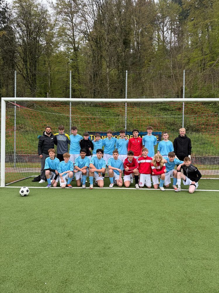 Soccer team posing in front of a goal on a field, wearing blue and red uniforms with coaches standing behind