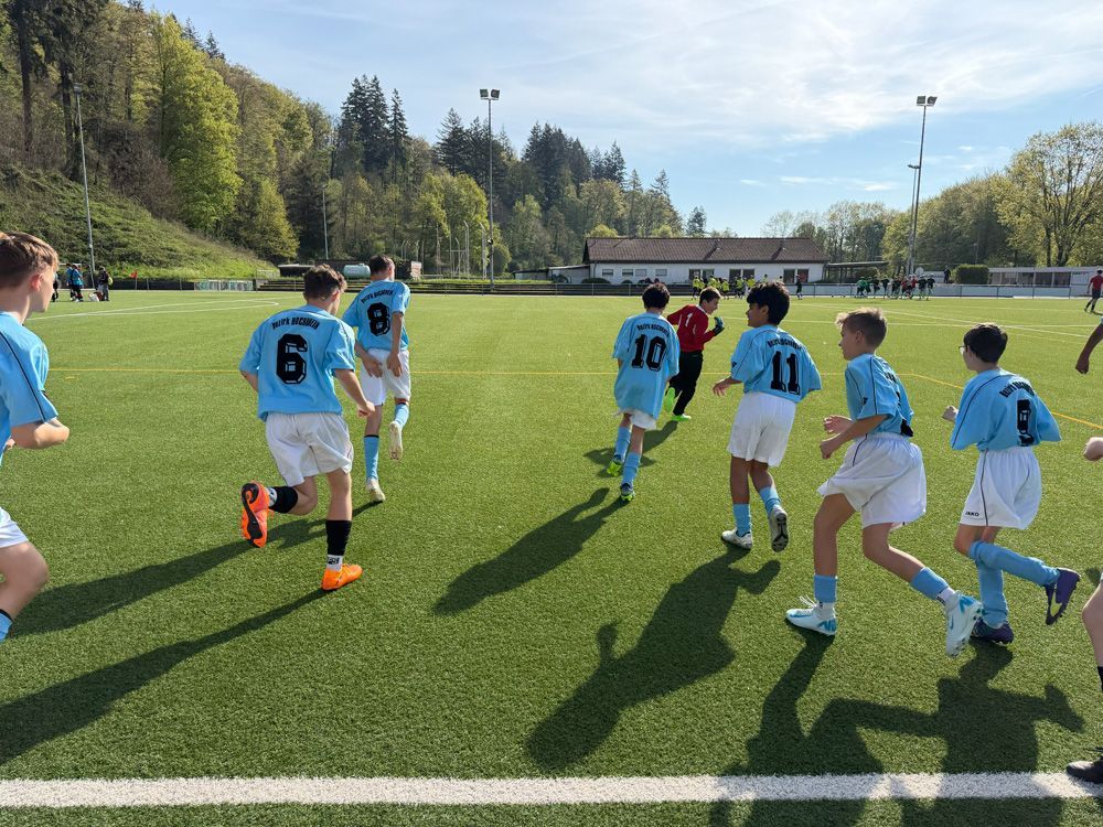 Children in light blue soccer jerseys running on a sunny outdoor field