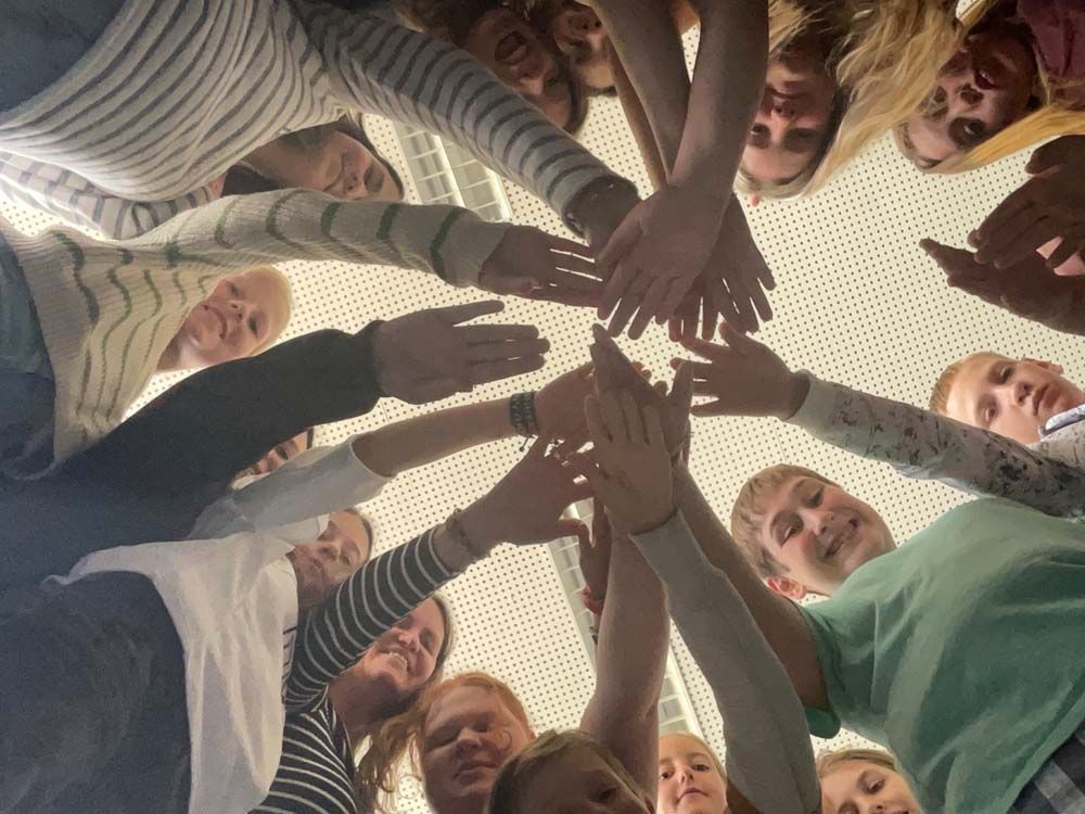 Gruppe von Menschen, die mit verschränkten Händen einen Kreis bilden, von unten betrachtet.