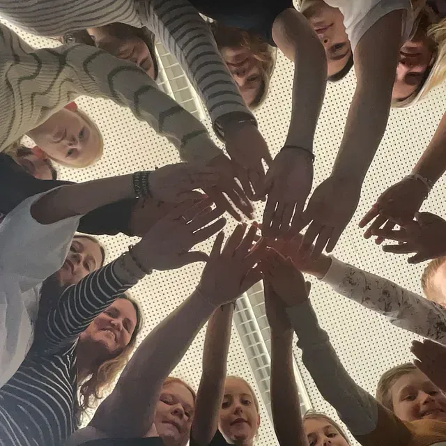 Gruppe von Menschen, die mit verschränkten Händen einen Kreis bilden, von unten betrachtet.