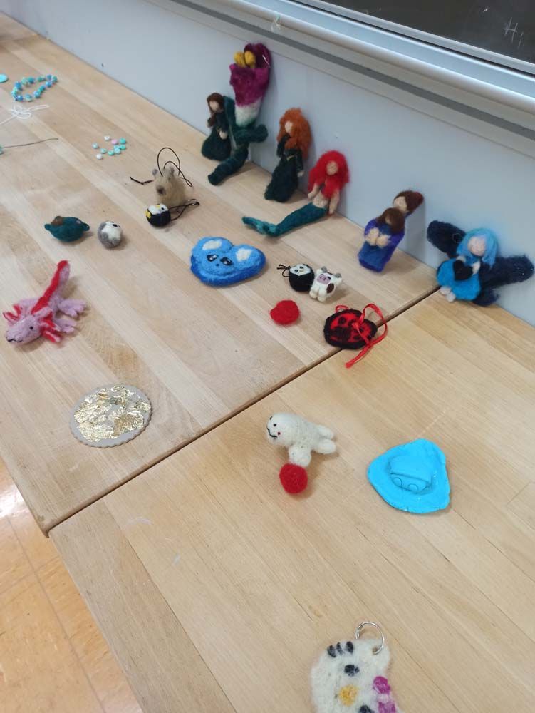 Handgefertigte Filzobjekte, arrangiert auf einer hellen Holzoberfläche, darunter Meerjungfrauen, Vögel und andere Figuren.