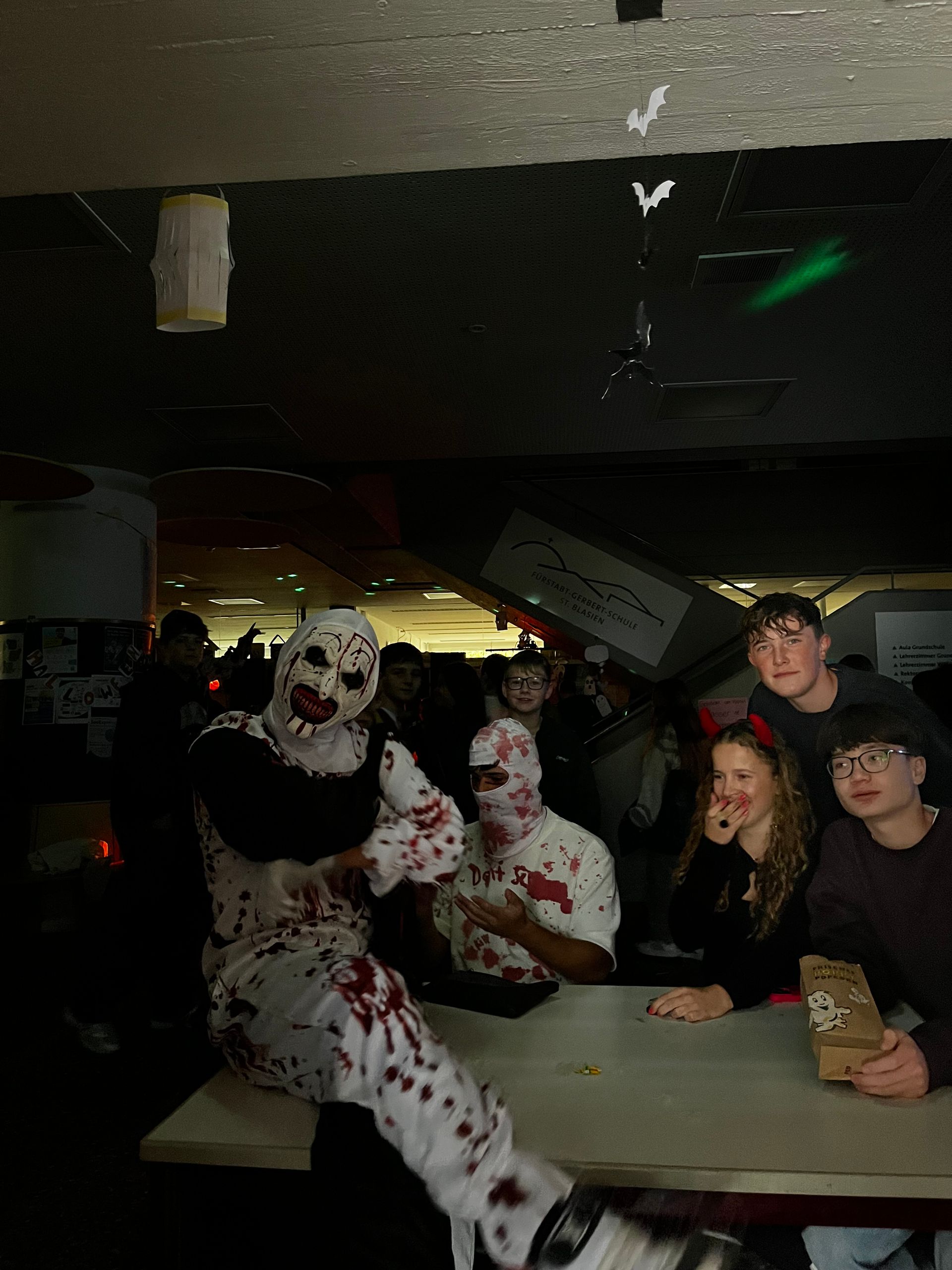 Clown und Zombie in Kostümen posieren mit Leuten. Blutspritzer auf den Kostümen. Dunkler Raum.