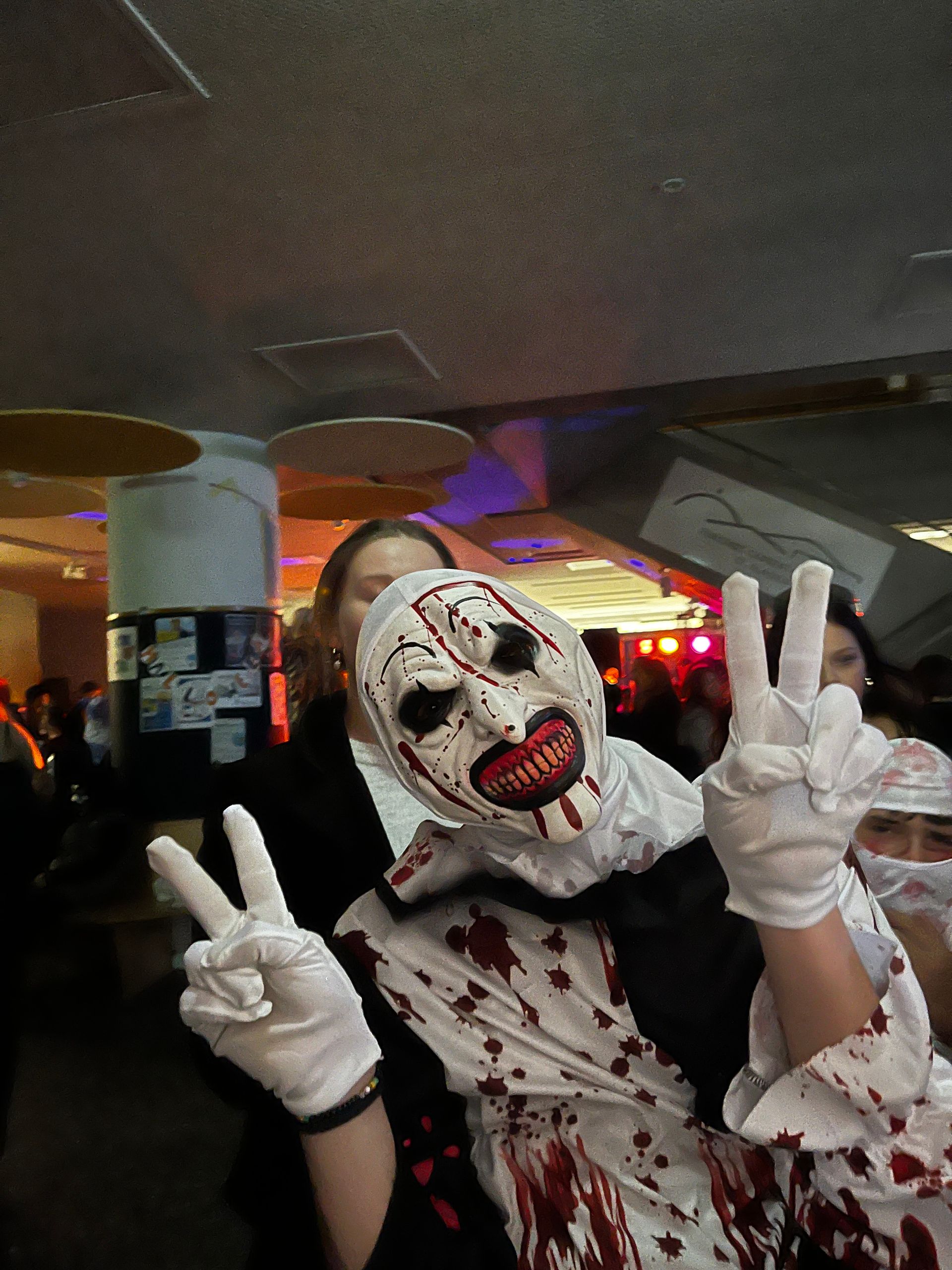 Person in blutigem Clownskostüm, die Friedenszeichen macht.