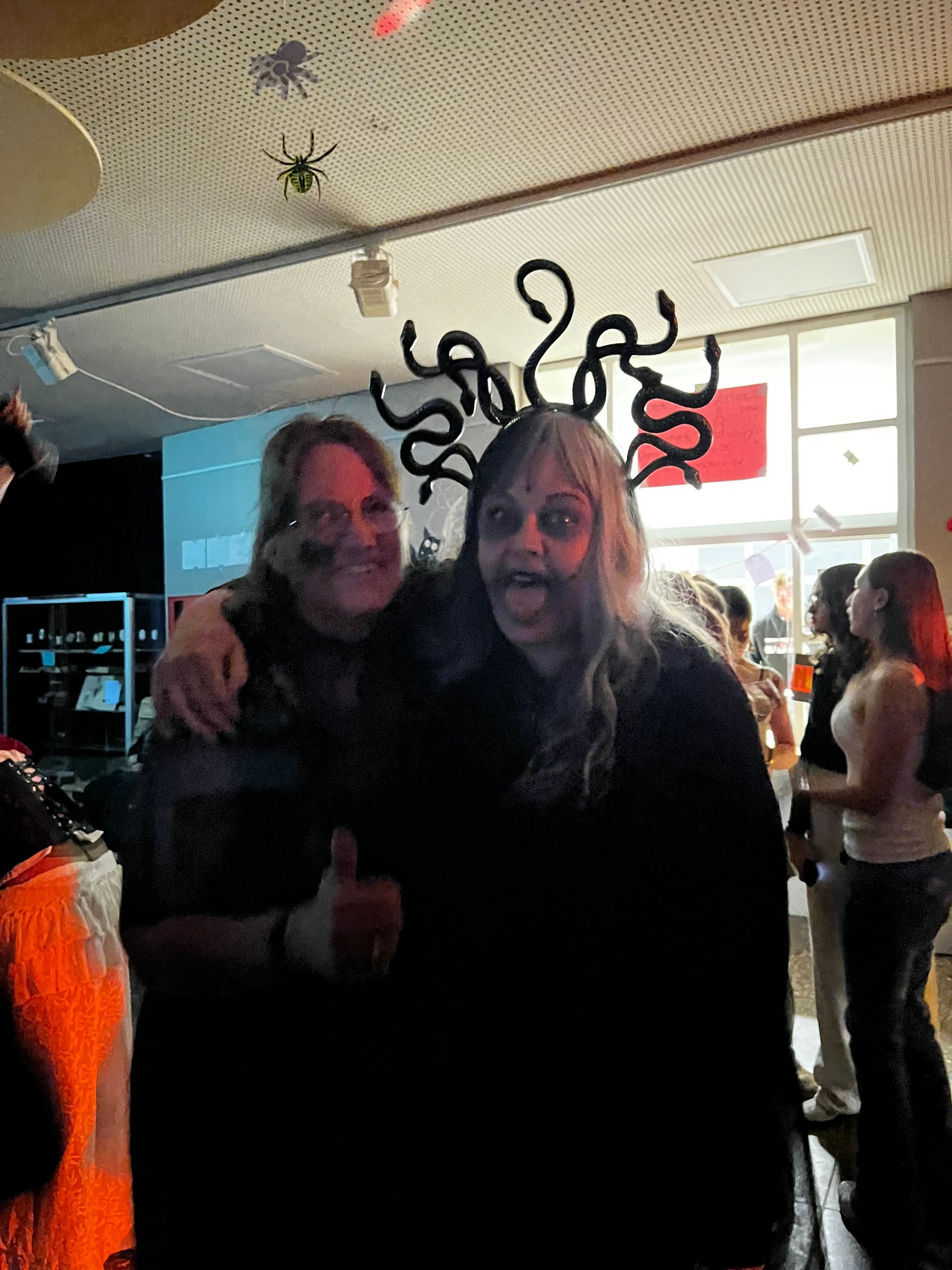 Zwei Personen in Halloween-Kostümen posieren in einem Innenraum; eine trägt einen Medusa-Kopfschmuck.