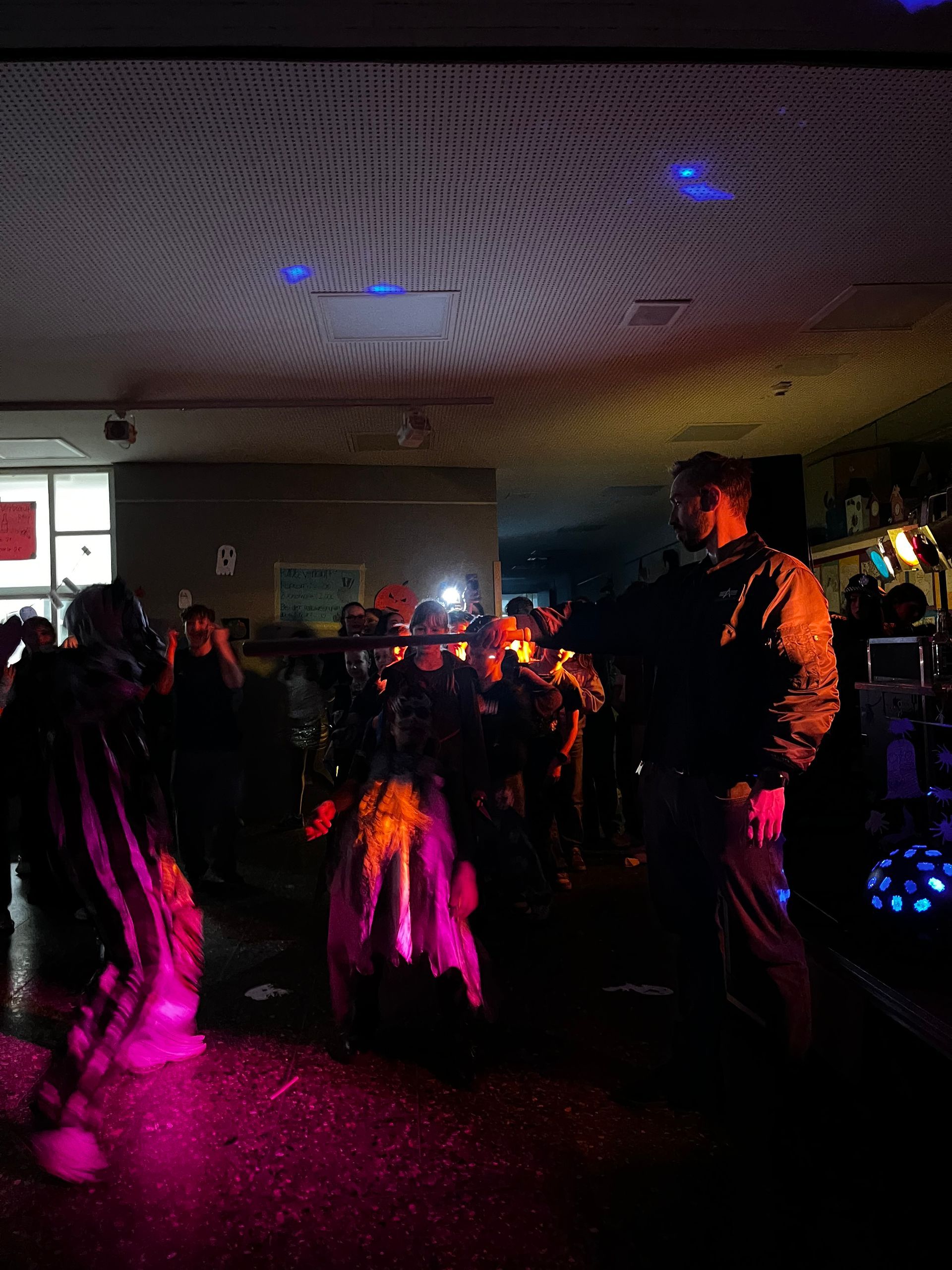 Menschen tanzen in einem schwach beleuchteten Raum mit rosa und blauen Lichtern. Einige halten Gegenstände in den Händen.