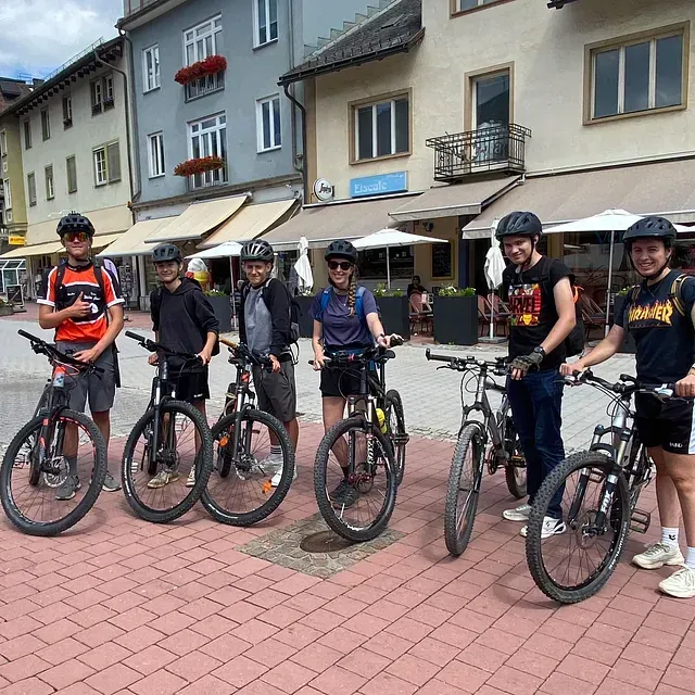 Eine Gruppe Radfahrer auf Fahrrädern auf einem europäischen Stadtplatz. Sie tragen Helme und posieren auf einem gepflasterten Platz.