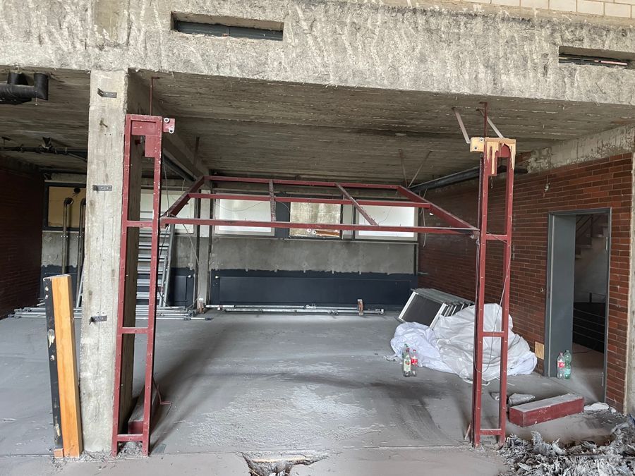 Innenansicht eines im Bau befindlichen Gebäudes mit rotem Metallgerüst und Betonkonstruktionen.