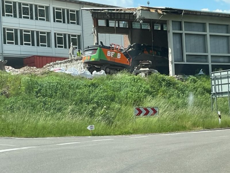 Abriss eines Gebäudes durch einen Bagger, Trümmer verstreut. Grün-weißes Gebäude. Blick von der Straße.