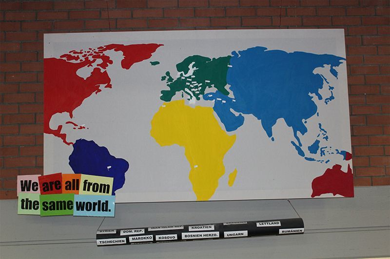 Farbenfrohe Weltkarte mit der Botschaft „Wir kommen alle aus derselben Welt“.
