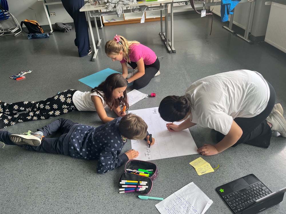 Kinder malen gemeinsam auf dem Boden in einem hell erleuchteten Raum.