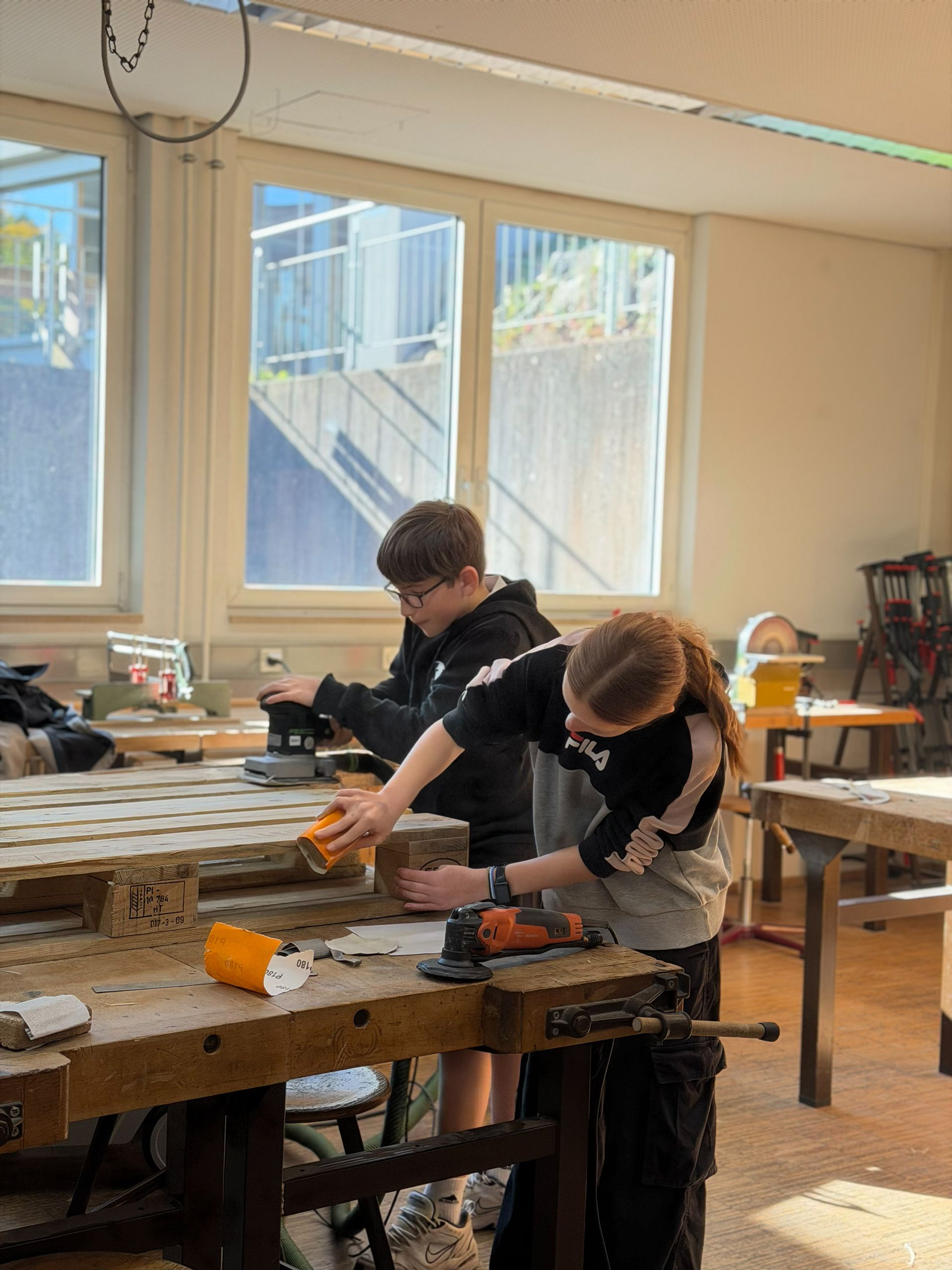 Zwei Schüler arbeiten an einem Werkstatttisch mit Holz und Werkzeugen.