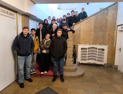 Eine Gruppe von Studenten posiert auf einer großen Treppe in einem Gebäude, einige auf den Stufen, andere oben, für ein Foto.