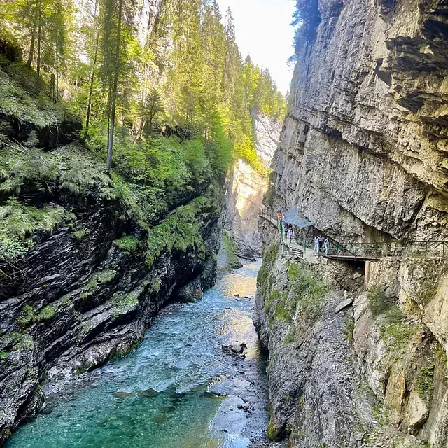 Tiefe, enge Schlucht mit einem türkisfarbenen Fluss und einem hölzernen Steg entlang der Felswand, gesäumt von Bäumen.