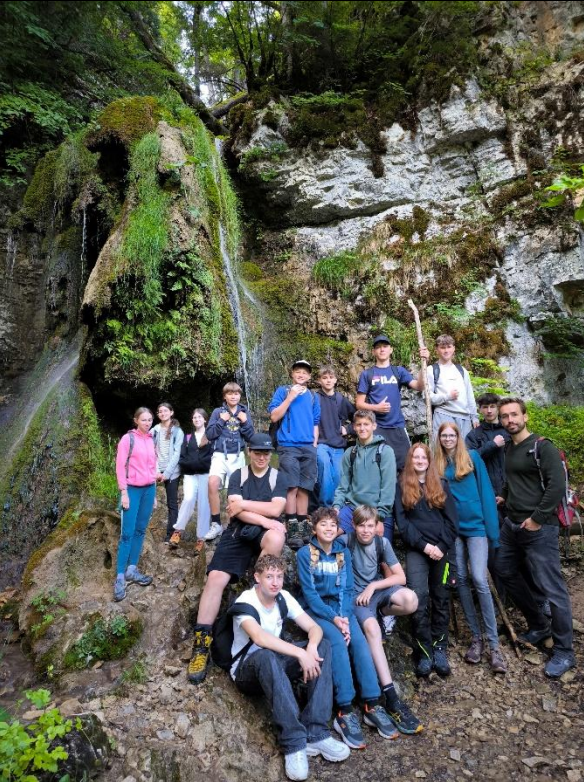 Eine Gruppe von Menschen posiert an einem Wasserfall in einem felsigen, bewaldeten Gebiet.