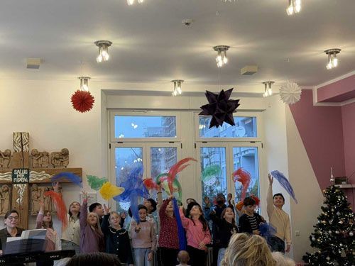 Eine Gruppe von Menschen schwenkt in einem Raum bunte Dekorationen; Weihnachtsbaum und Dekorationen sind zu sehen.