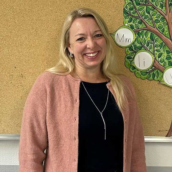 Eine lächelnde Frau in rosa Strickjacke und schwarzem Oberteil steht neben einem Baumdiagramm.