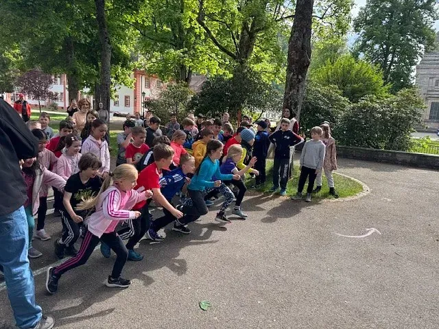 Kinder an der Startlinie, bereit zum Loslaufen. Freiluftkulisse mit Bäumen und Gebäuden im Hintergrund.