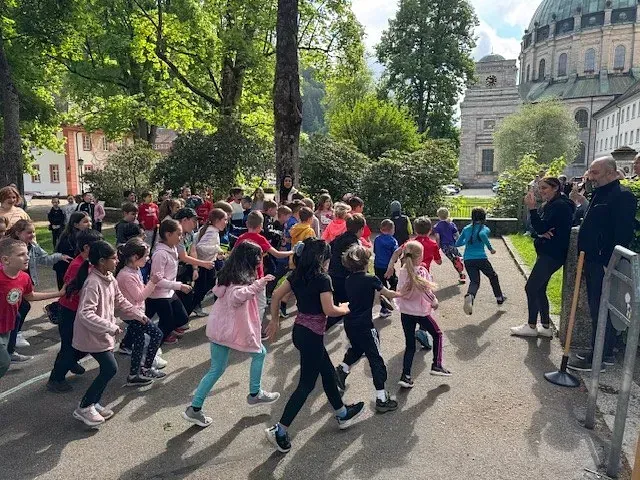 Eine Gruppe Kinder treibt Sport im Freien; im Hintergrund ist ein historisches Gebäude zu sehen.