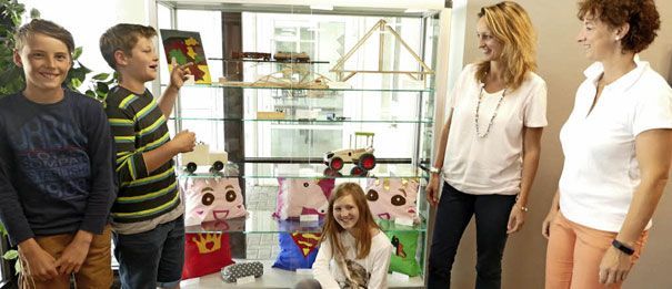 Zwei Jungen und ein Mädchen stehen mit zwei Frauen an einer Vitrine mit Kissen und Spielzeug.