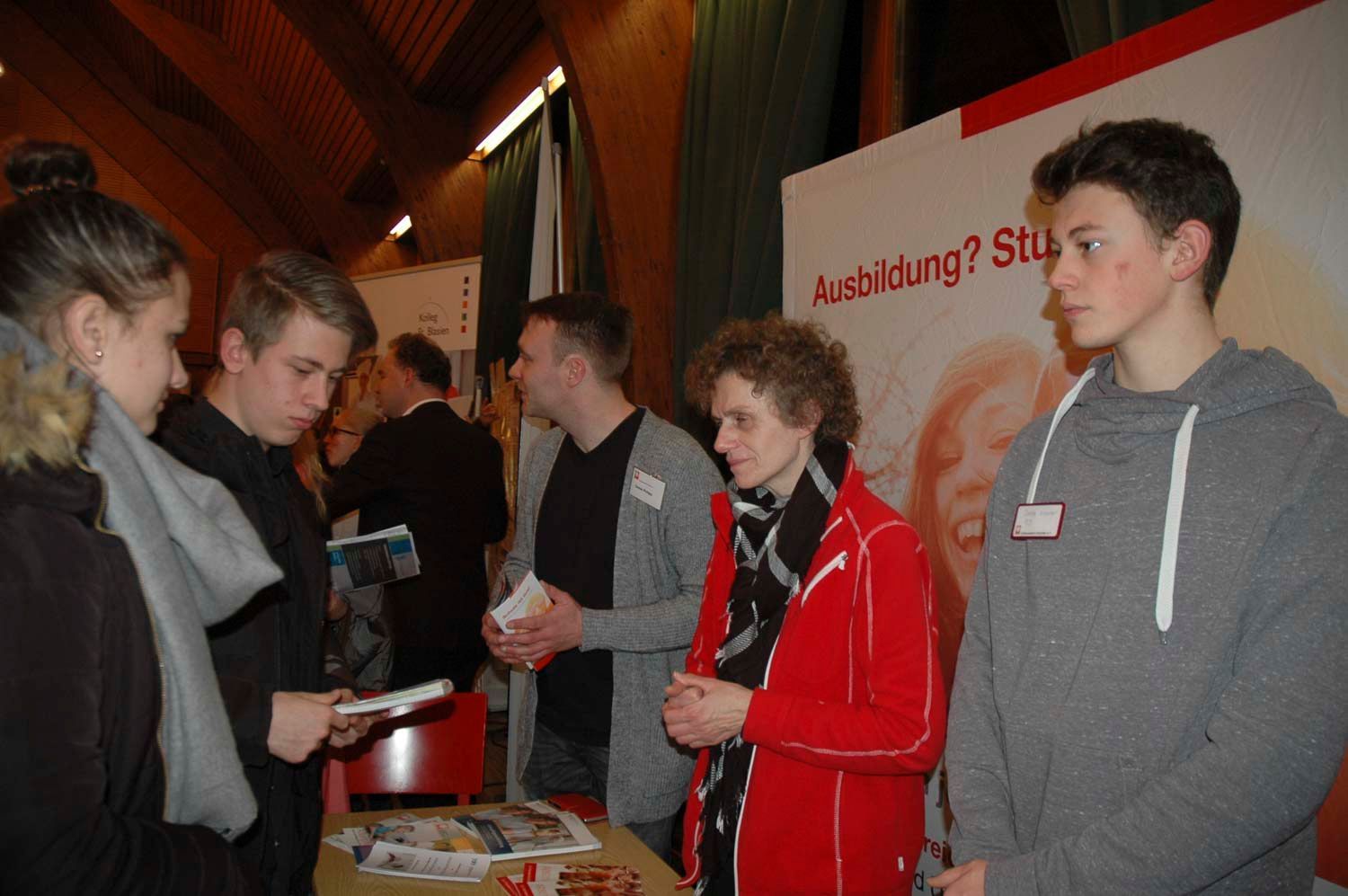 Eine Gruppe von Menschen auf einer Karrieremesse; sie betrachten Broschüren und Stände mit Werbematerialien.