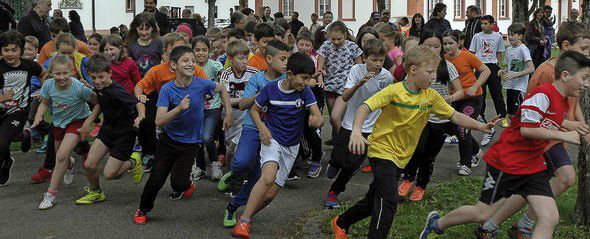 Eine Gruppe Kinder rennt umher, einige tragen bunte Kleidung, in der Nähe eines Gebäudes mit Fenstern.