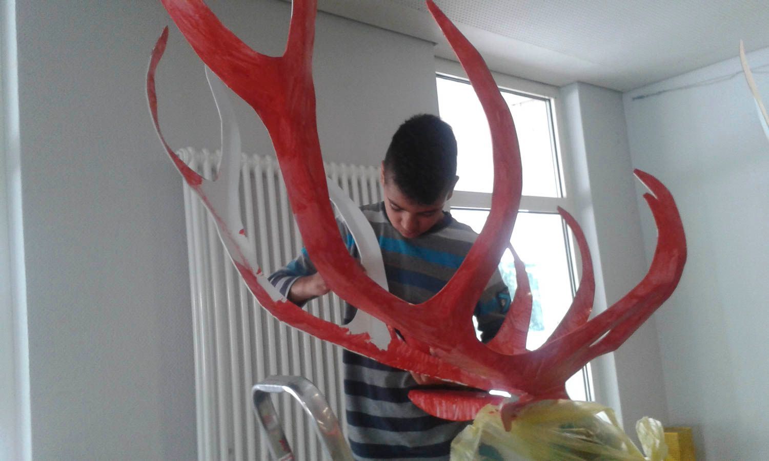 Ein Junge bemalt ein rotes Geweih, das an einer Skulptur in einem Innenraum befestigt ist.
