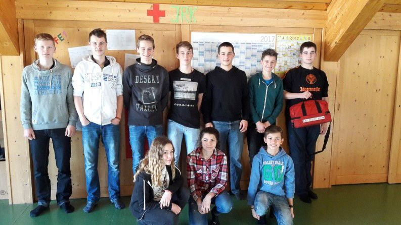 Eine Gruppe von zehn Personen posiert vor einer holzgetäfelten Wand mit einem Erste-Hilfe-Symbol.