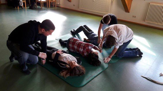 Vier Personen üben Erste Hilfe an Patienten, die in einem Raum auf einer Matte liegen.