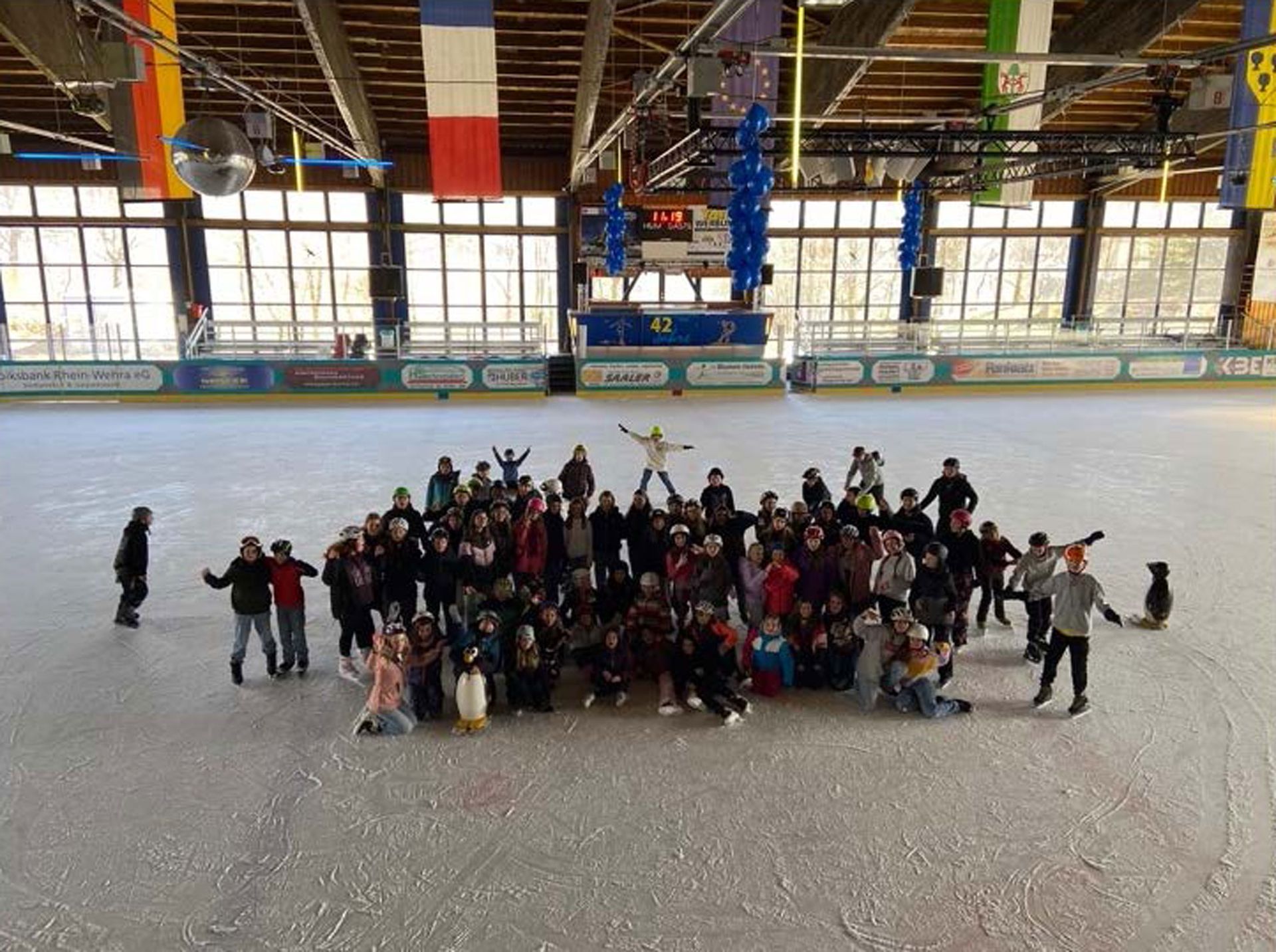 Eine Gruppe von Menschen auf einer Eisbahn, viele mit erhobenen Armen. Fahnen hängen von der Decke.