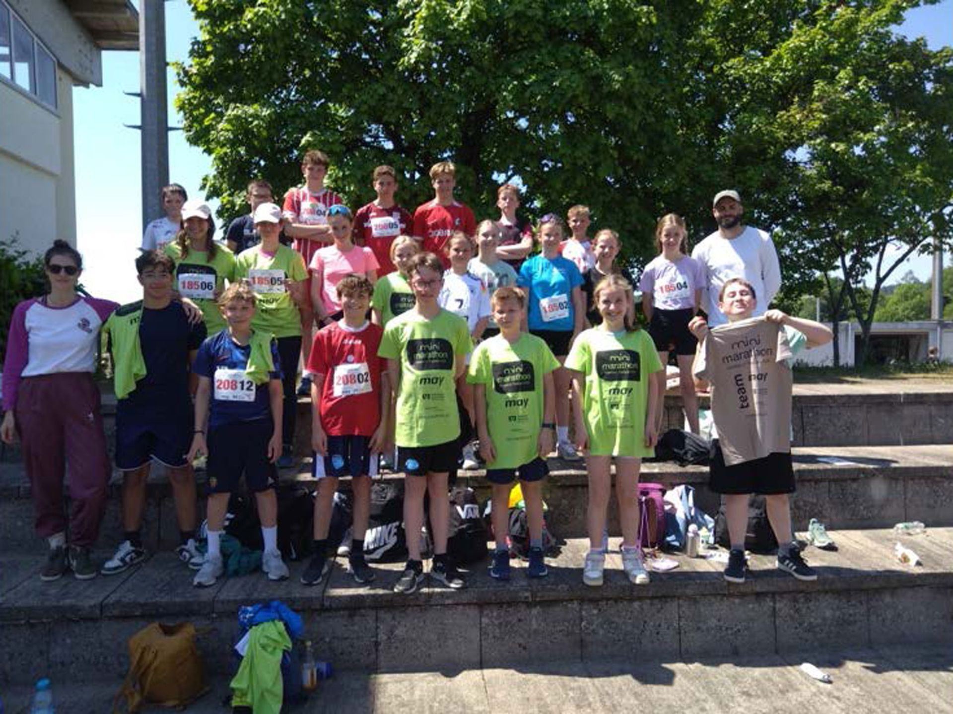 Eine Gruppe von Menschen in Laufkleidung posiert draußen auf einer Treppe. Einige halten T-Shirts in der Hand.