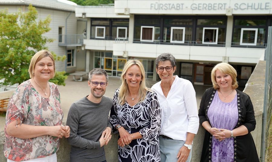 Fünf Erwachsene posieren vor einem Schulgebäude.