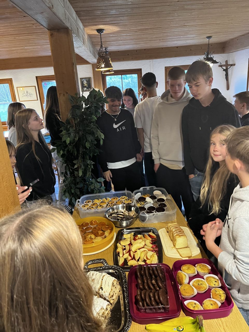 In einem Raum mit Holzbalken und einem Fenster versammelten sich die Menschen um einen reich gedeckten Tisch.