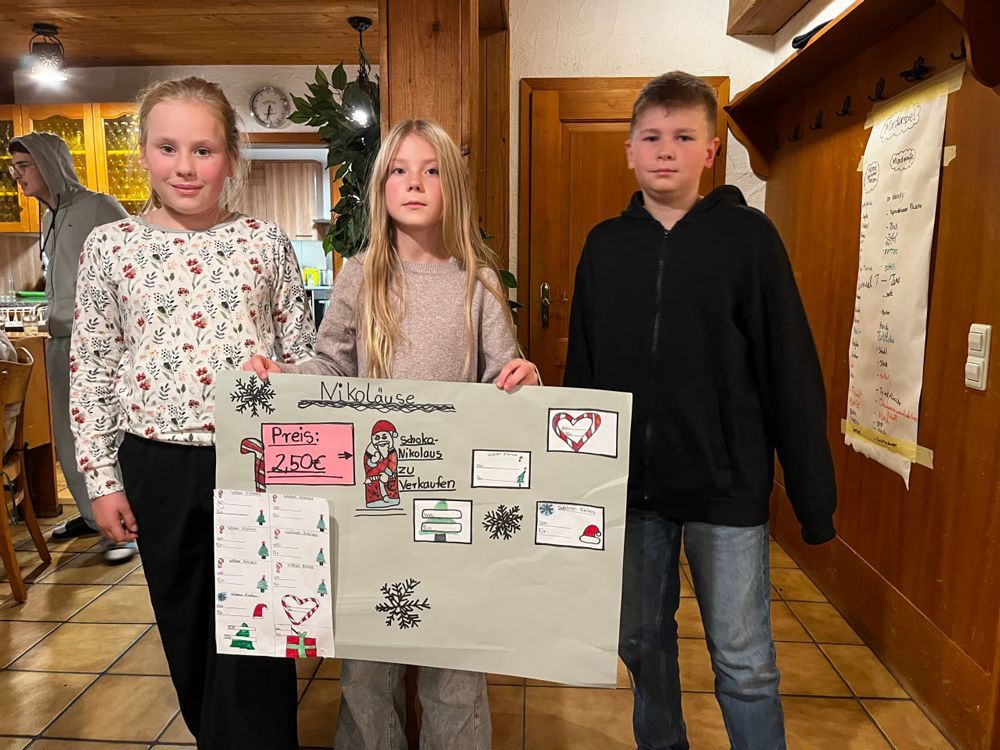 Drei Kinder halten drinnen ein selbstgemaltes Plakat und lächeln.