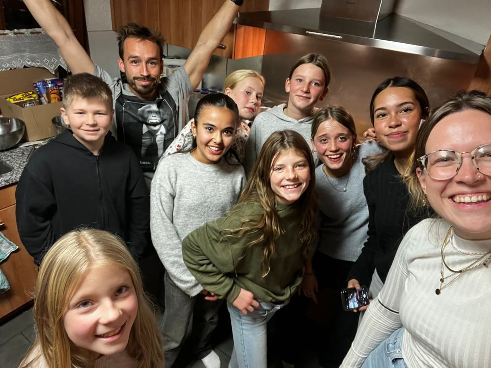 Eine Gruppe lächelnder Menschen in einer Küche; einige schauen in die Kamera, eine Person hat die Arme erhoben.