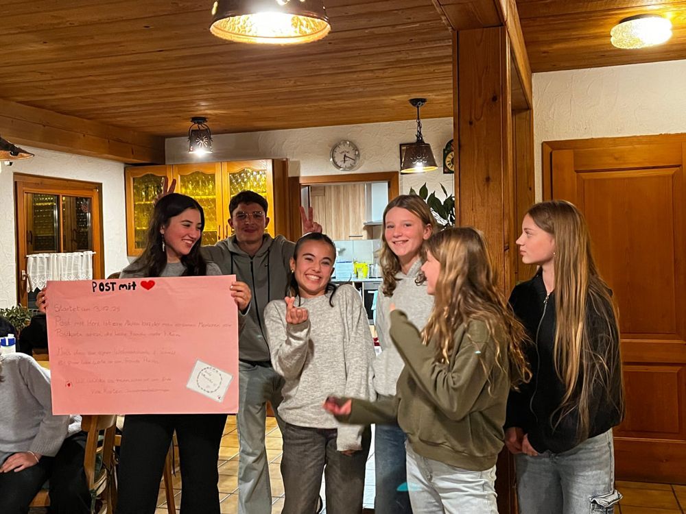 Eine Gruppe von Menschen hält ein rosa Schild in einem holzgetäfelten Raum. Einige lächeln und gestikulieren.