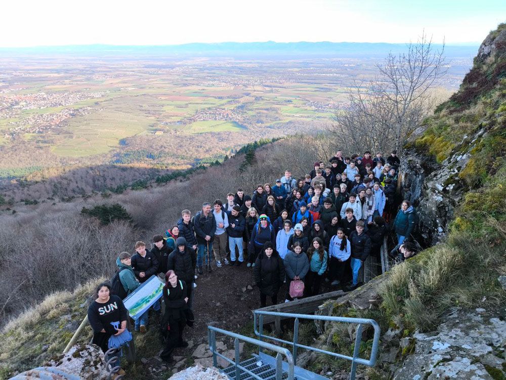 Eine große Gruppe von Studenten posiert auf einem Hügel mit malerischem Blick ins Tal.