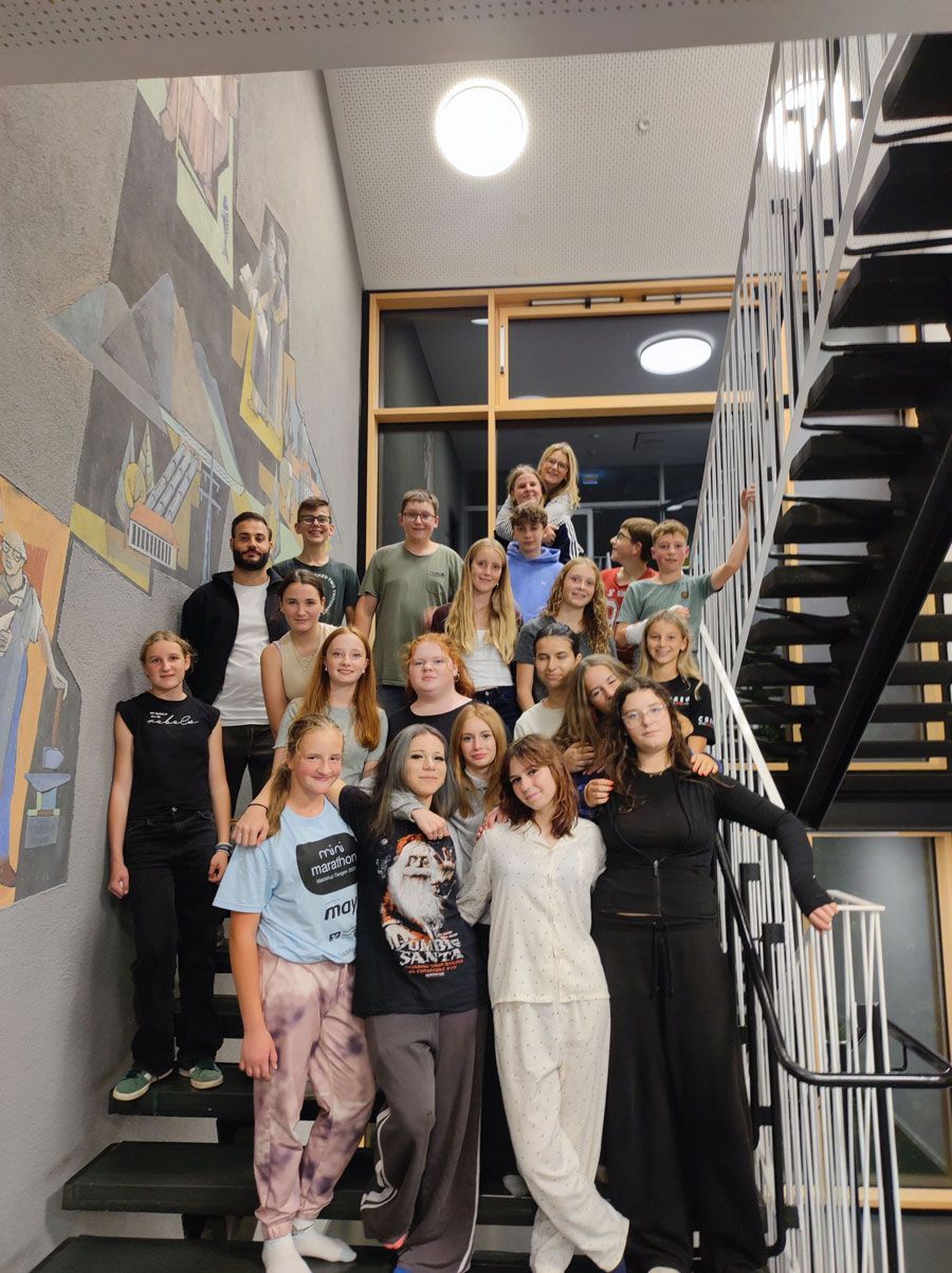 Group of people posing on a stairwell in a modern building, with black stairs and wall art.