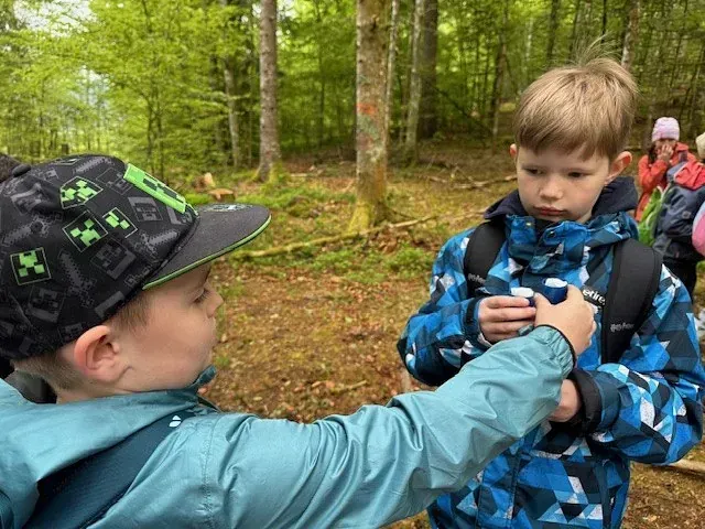 Zwei Jungen im Wald, einer rückt den Rucksack des anderen zurecht. Der Junge links trägt eine Minecraft-Mütze.
