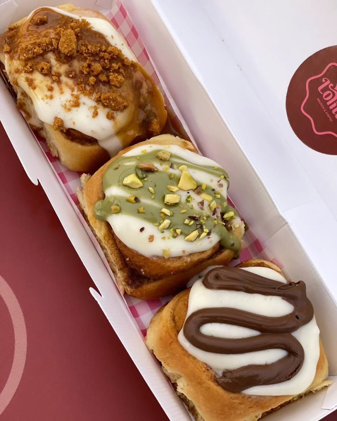 Tres pasteles glaseados en una caja rosa: caramelo, pistacho y chocolate con sirope.