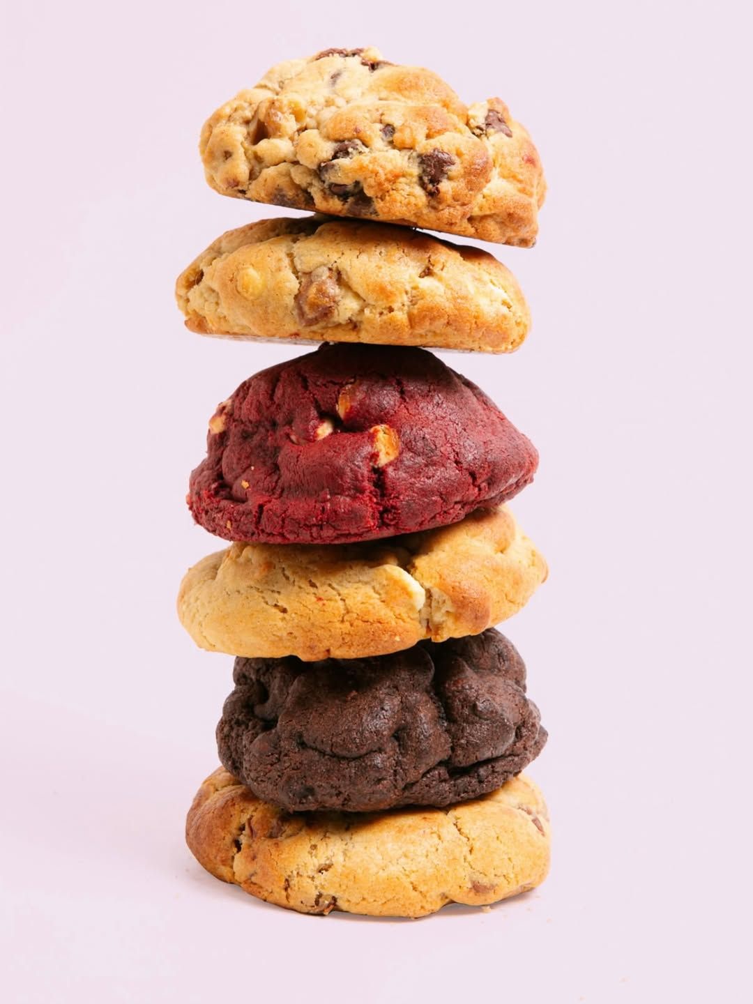 Pila de cinco galletas variadas sobre un fondo rosa.