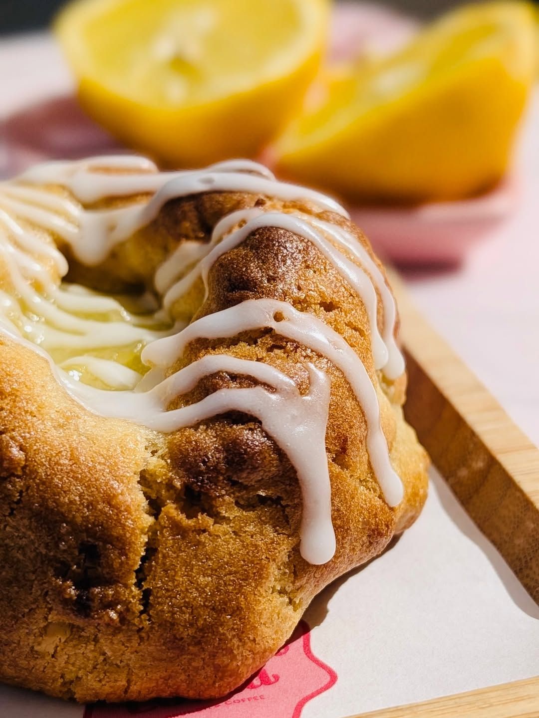 Rollo de canela glaseado en un plato con rodajas de limón al fondo.