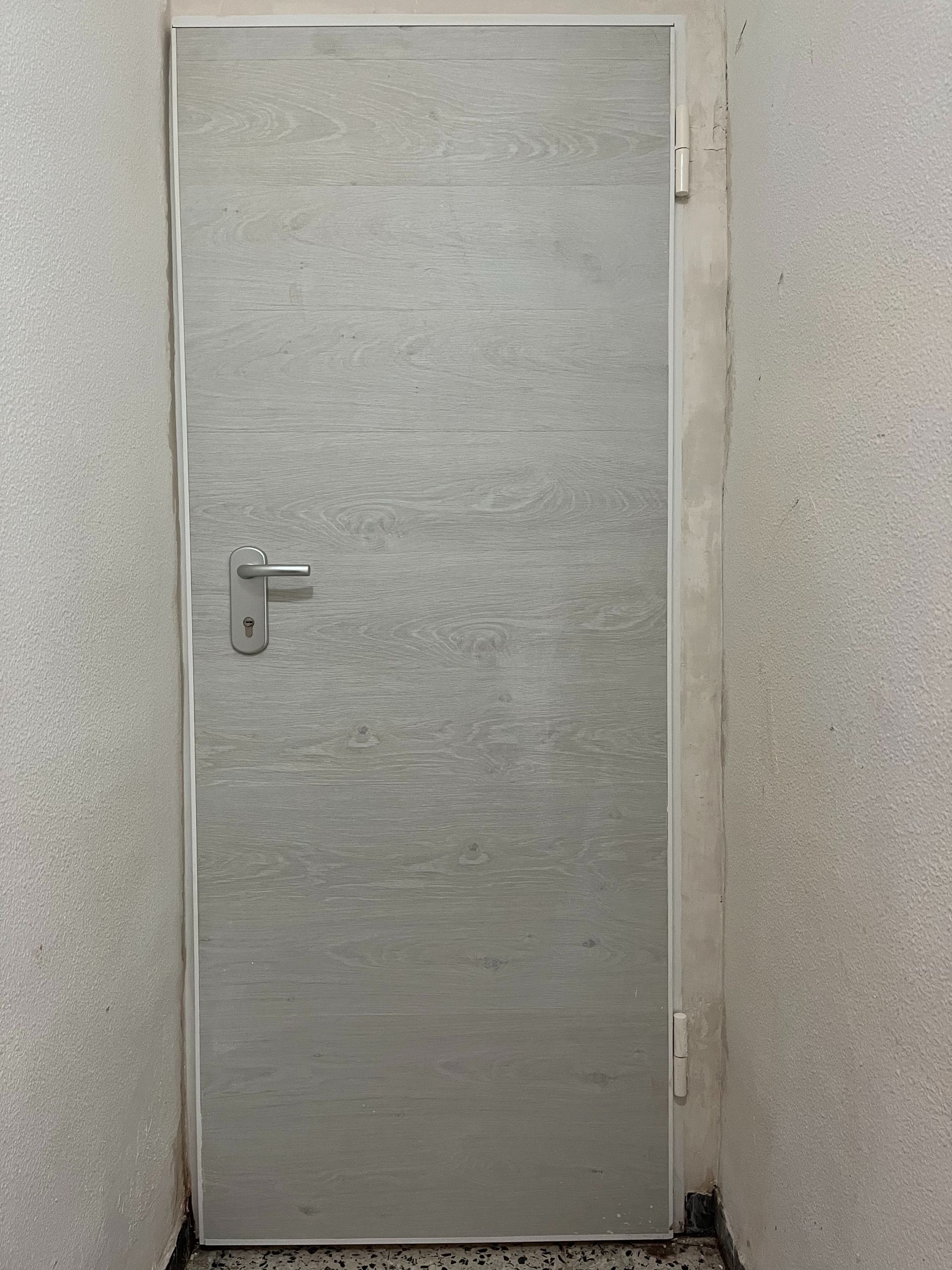 En un pasillo hay una puerta blanca con tirador.