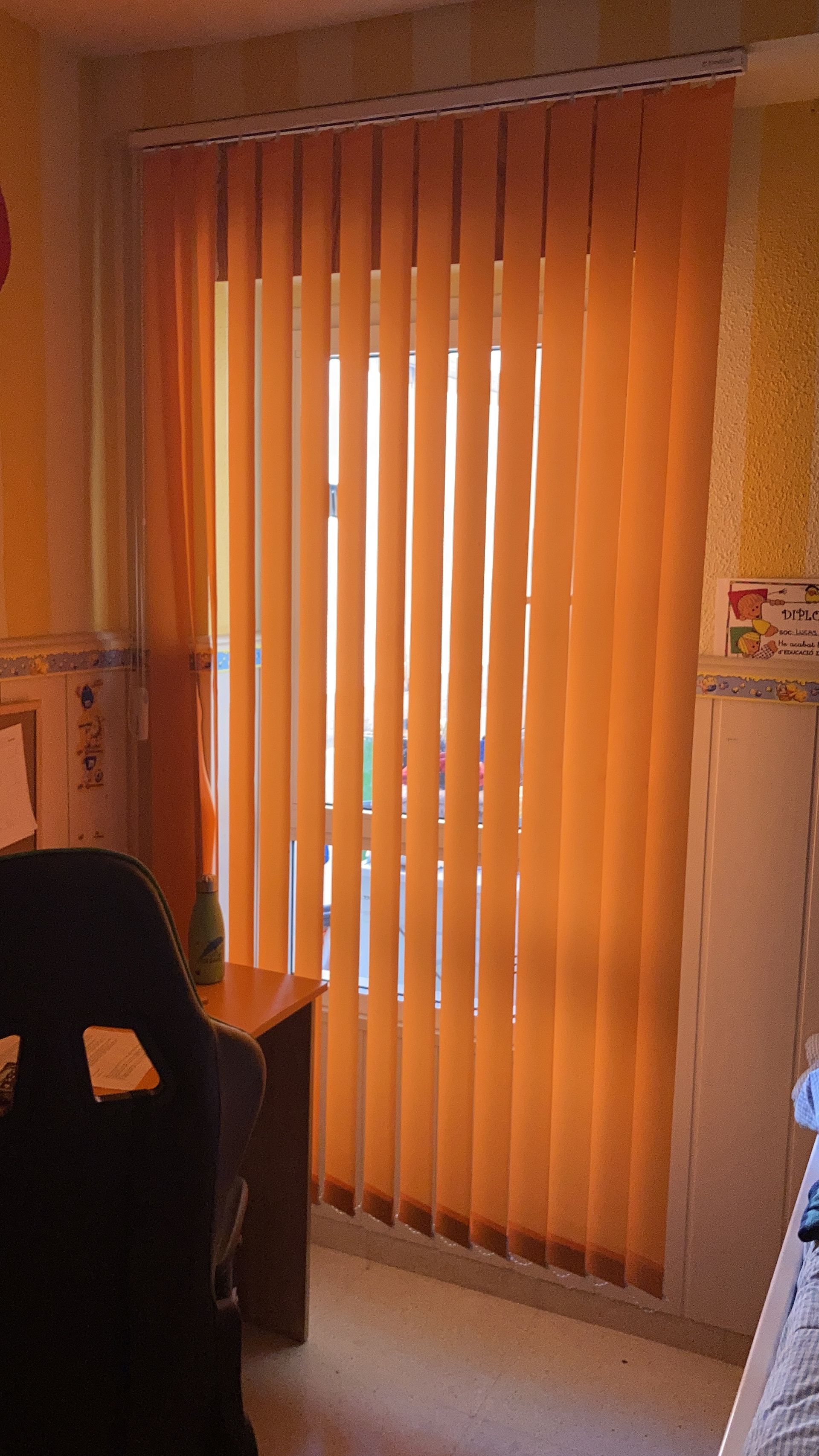 Una habitación con persianas verticales naranjas en una ventana.